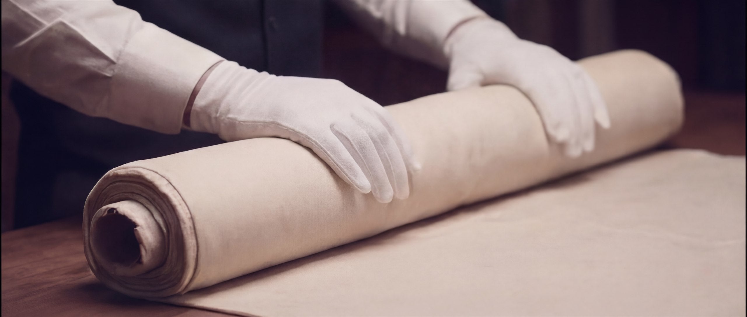 White-gloved hands reviewing a roll of material before preservation work begins.