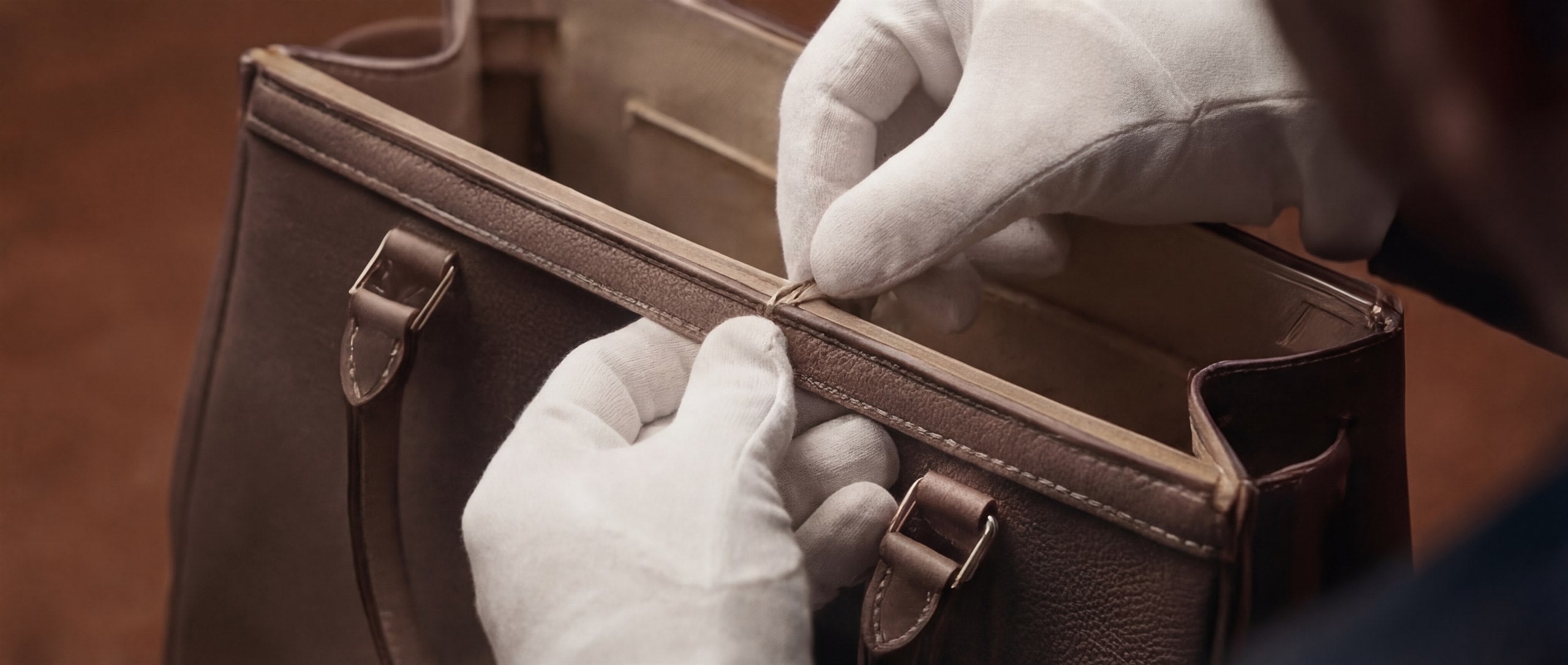White-gloved hands restoring the upper edge and structural finish of a leather bag.